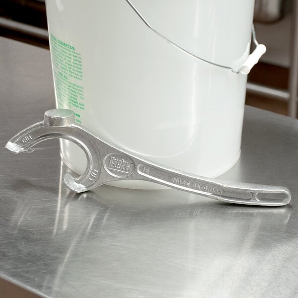 A silver Tablecraft pail opener next to a white metal bucket.
