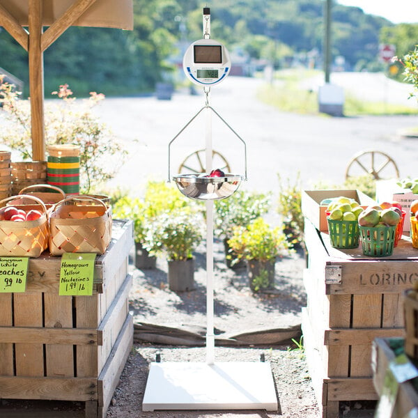 A Cardinal Detecto hanging scale with a basket of fruit on a stand.