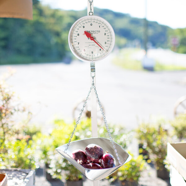 A Cardinal Detecto hanging scale with a metal scoop of onions.
