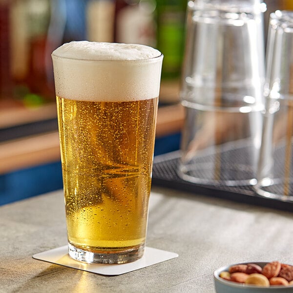 A Libbey stackable mixing glass of beer on a table with foam on top.