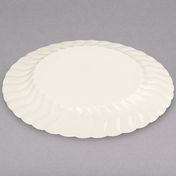 A Fineline Flairware ivory plastic plate with a wavy design on a gray surface.