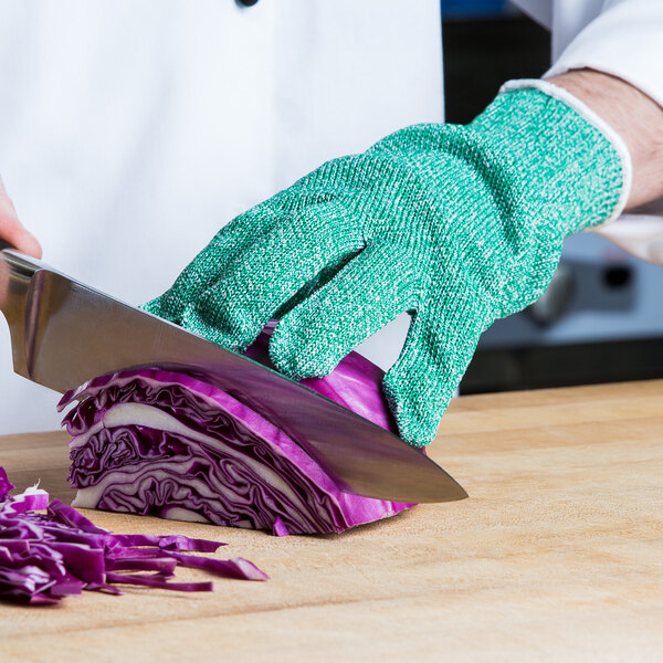A person wearing a San Jamar green cut resistant glove cutting cabbage on a table.