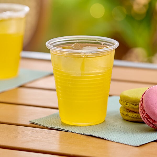 A Choice translucent plastic cup filled with yellow liquid next to pink and yellow macaroons.