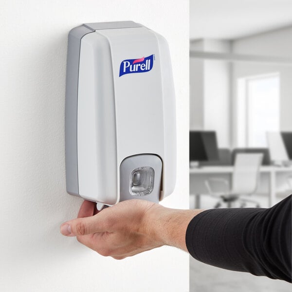 A person using a Purell hand sanitizer dispenser on a wall.