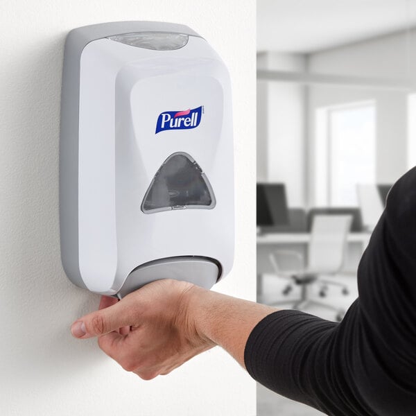 A person using a Purell hand sanitizer dispenser.