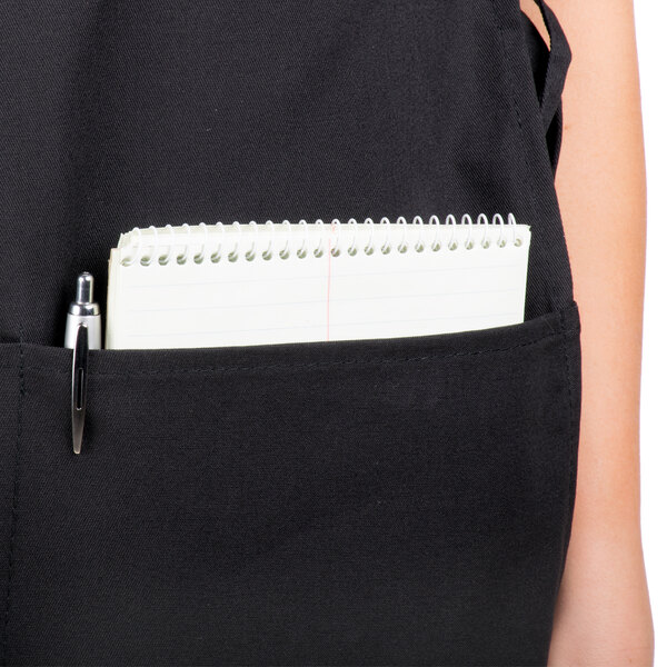A person wearing a black Intedge cobbler apron with a notebook and pen in the pocket.