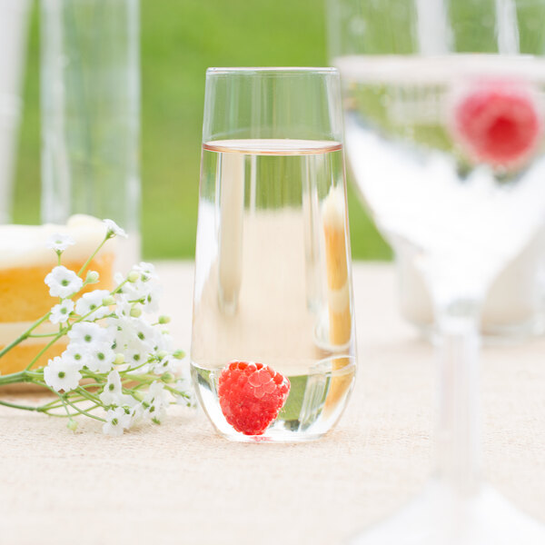 A WNA Comet clear plastic stemless flute filled with a clear liquid and a raspberry.