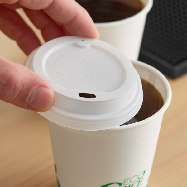A white compostable paper hot cup lid being placed on a paper cup filled with coffee.
