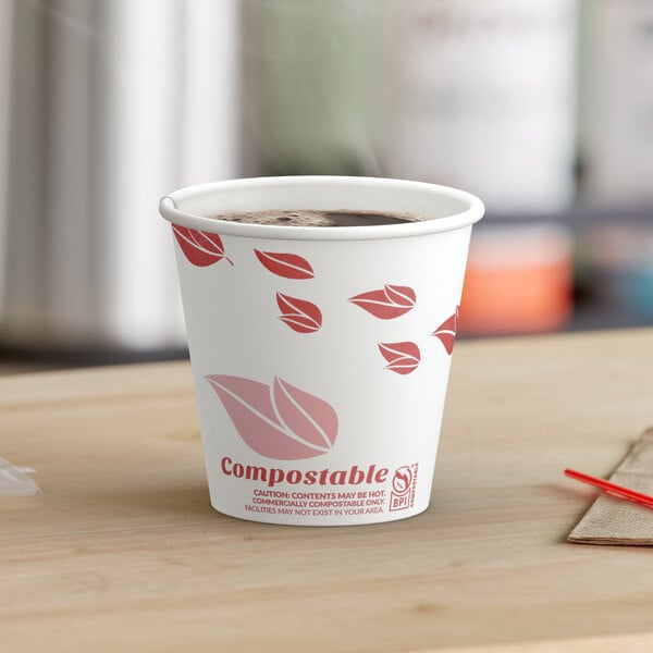 A close-up of a EcoChoice paper hot cup of coffee with red leaves on it.