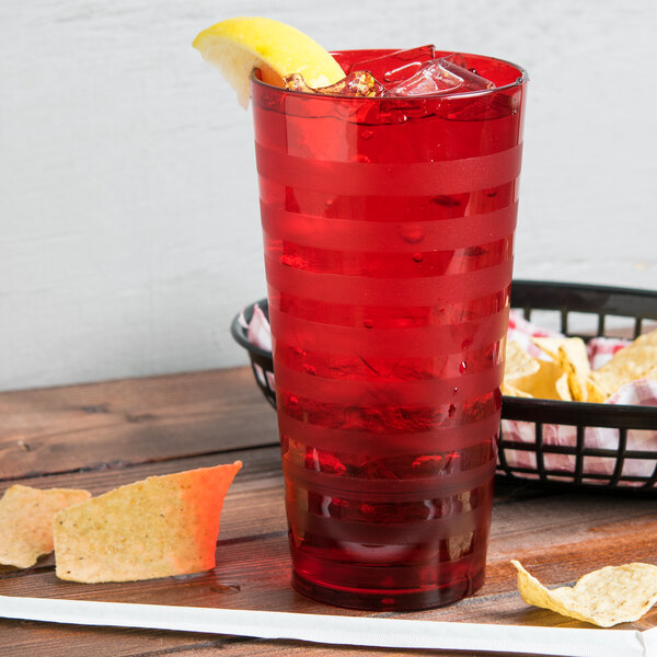 A red Orbis plastic tumbler filled with red liquid on a table with chips and salsa.