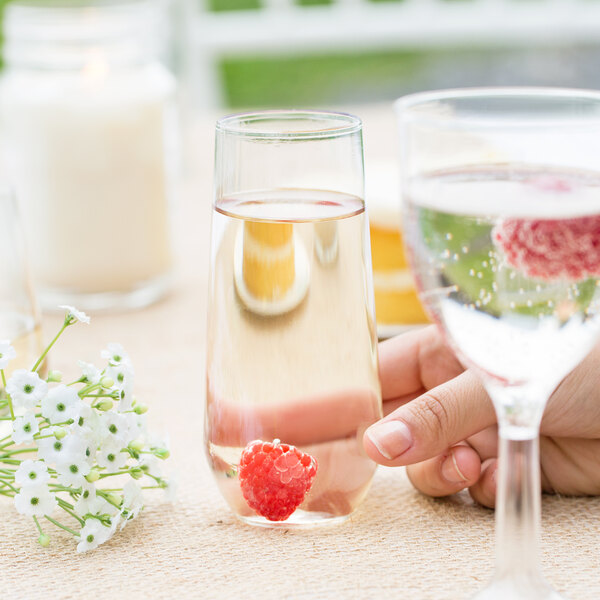 A hand holding a WNA Comet clear plastic stemless flute with a raspberry in it.