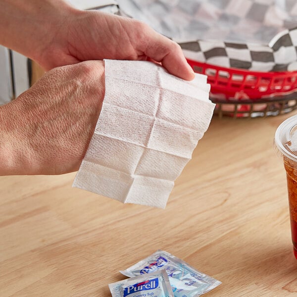 A hand wipes a table with a Purell Cottony Soft Sanitizing Wipe.