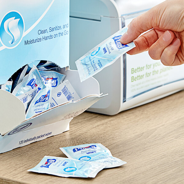 A hand putting a packet of Purell Cottony Soft Sanitizing Wipes into a dispenser.