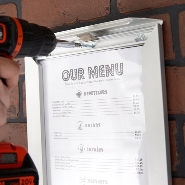 A hand using a screwdriver to attach a menu to a Aarco satin aluminum snap frame.