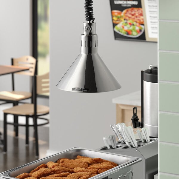 A kitchen with a large tray of food and a Hatco hanging heat lamp over it.