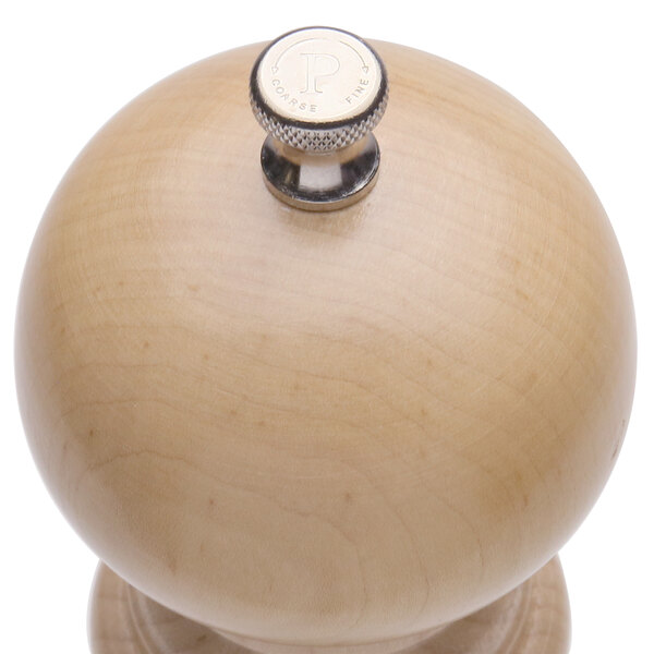 A close-up of a silver knob on a wooden pepper mill.
