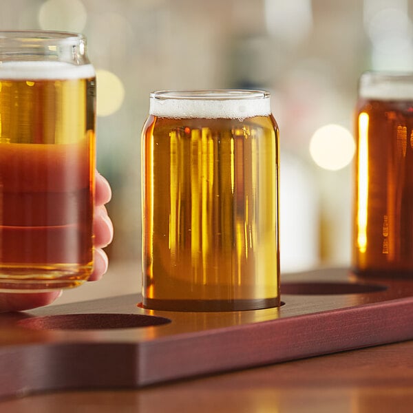 A person holding a Libbey beer tasting glass filled with beer.