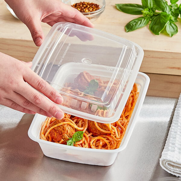 A hand holding a Choice white rectangular microwavable container filled with spaghetti and meatballs.