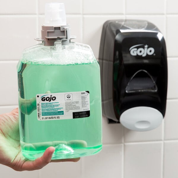 A hand holding a bottle of green GOJO Cucumber Melon foaming hand, hair, and body wash.