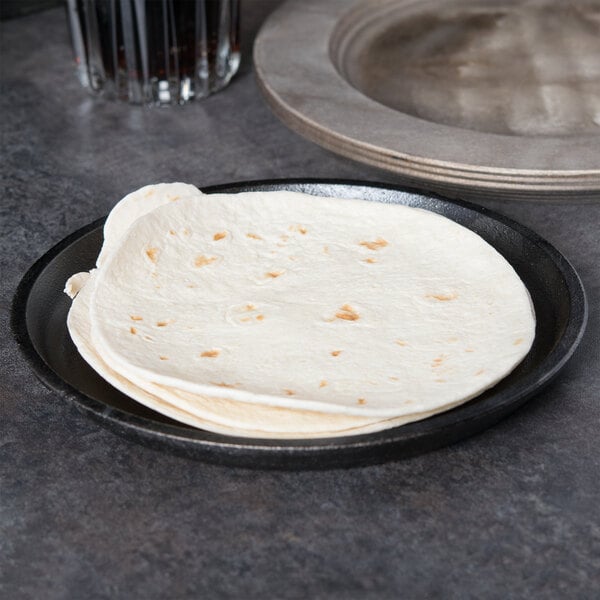 A Lodge pre-seasoned cast iron fajita skillet with tortillas on a plate.