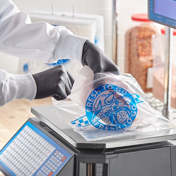 A person in gloves in a professional kitchen using a Choice Deli Saddle Bag Stand to put food in a printed plastic bag.