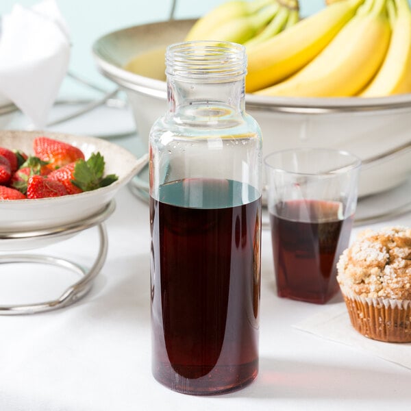 A Cal-Mil polycarbonate bottle filled with liquid on a table with a bowl of strawberries and muffins.