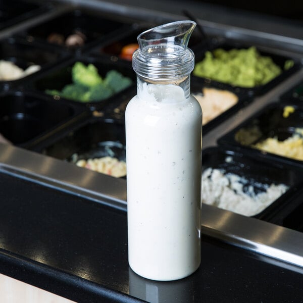 A Cal-Mil polycarbonate salad dressing bottle with a blue lid filled with white liquid on a counter.