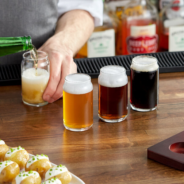 A man pouring dark beer into Libbey tasting glasses on a table in a bar.