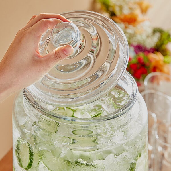 A hand using an Acopa glass jar with a lid to dispense cucumber water.