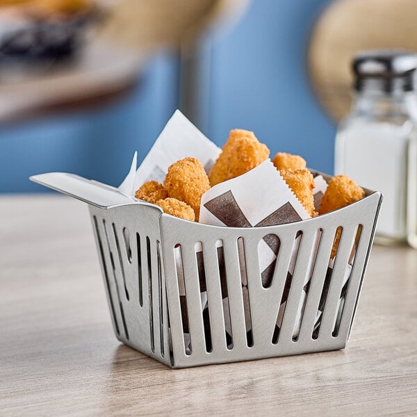 A Tablecraft stainless steel side French fry basket filled with fried chicken nuggets on a table.