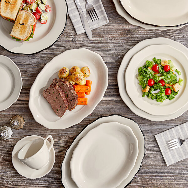 An Acopa ivory scalloped stoneware plate on a wood surface with a plate of meat and vegetables.