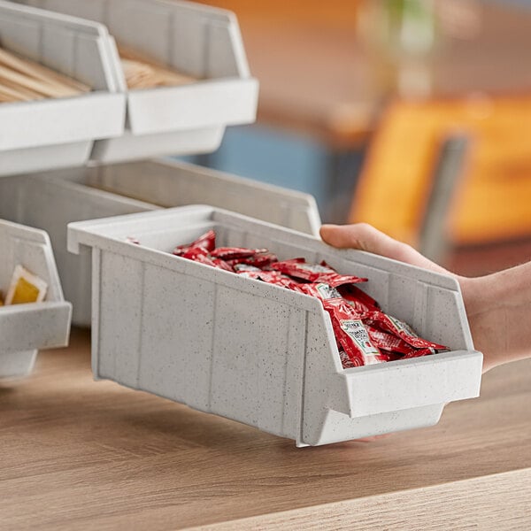 A hand holding a Cambro speckled gray organizer bin full of condiments.