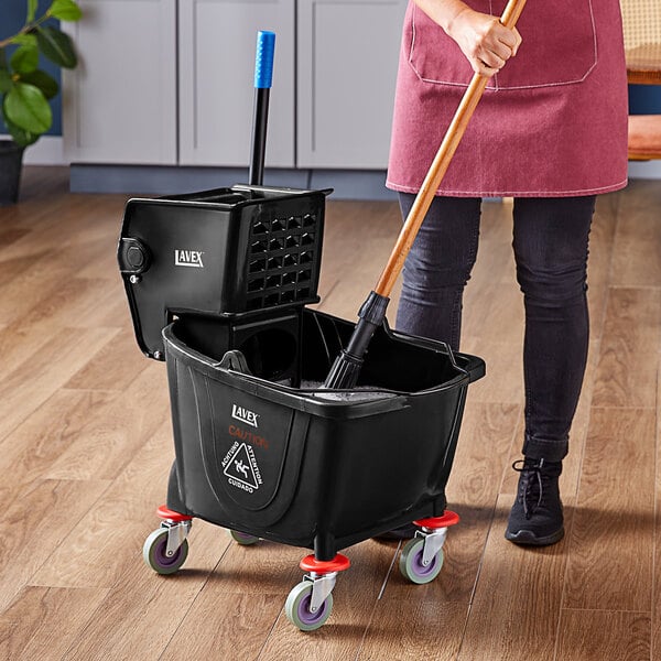 A woman holding a Lavex black mop bucket with a handle and a mop.