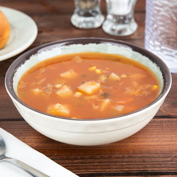 A Carlisle jade melamine bowl filled with soup on a table with a roll and silverware.