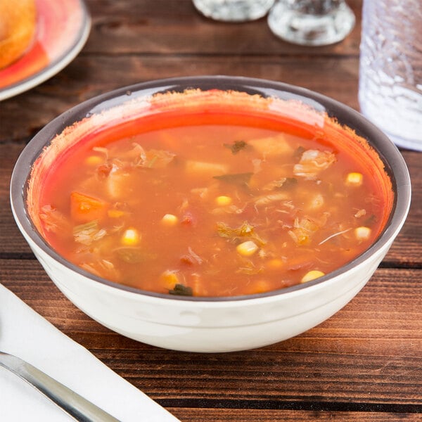 A Carlisle Fireball melamine bowl filled with soup, vegetables, and herbs on a table.