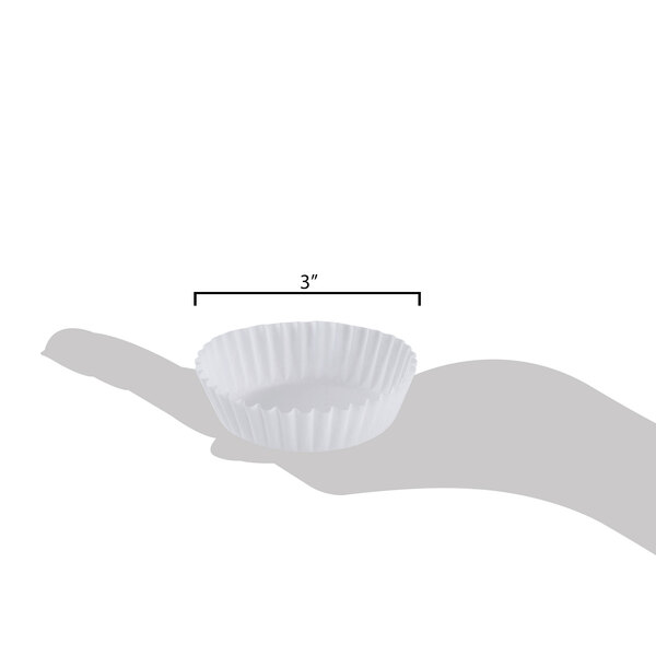 A hand holding a white fluted mini baking cup with a measurement on it.