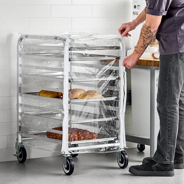 A clear plastic bun pan rack cover with three zippers fitted over a metal rack holding trays of baked goods.
