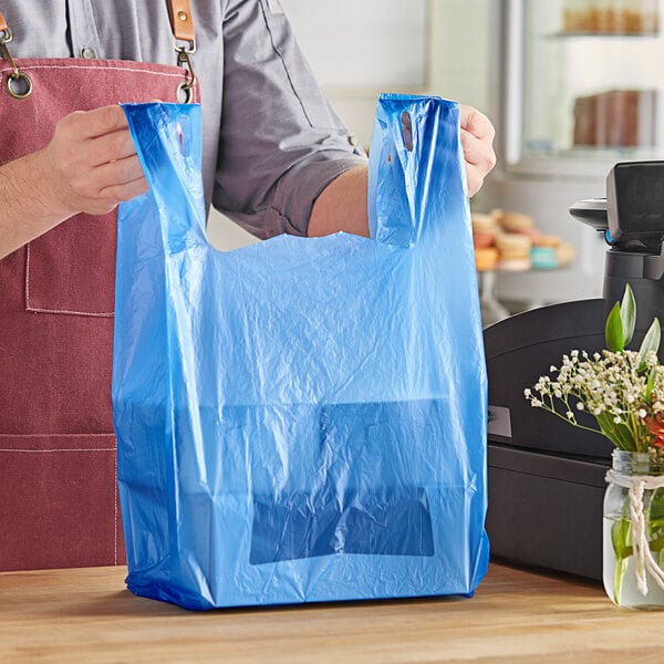 A man holding a blue plastic Choice Standard-Duty T-Shirt bag with a vase of flowers