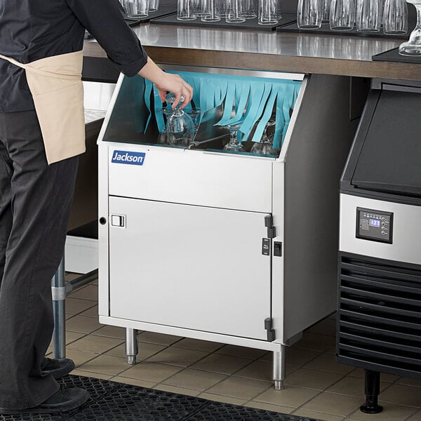 A person putting a glass in a Jackson DELTA carousel glass washer.