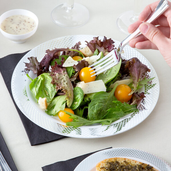 A person holding a Visions plastic fork over a salad on a table.