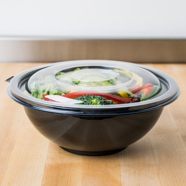 A Fineline clear plastic bowl with a lid on a wood surface filled with food.