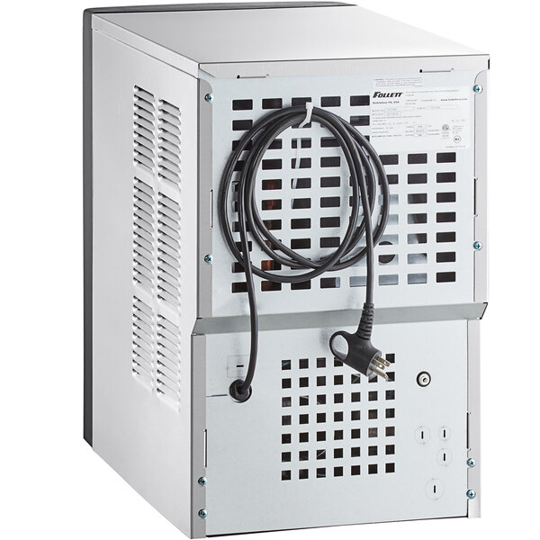 A white rectangular Follett countertop ice maker and water dispenser with a black cord attached.