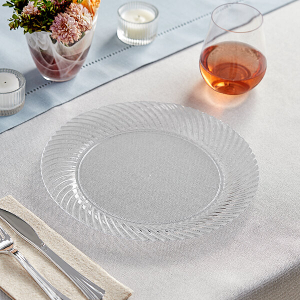 A Visions clear plastic plate with silverware on a white table.