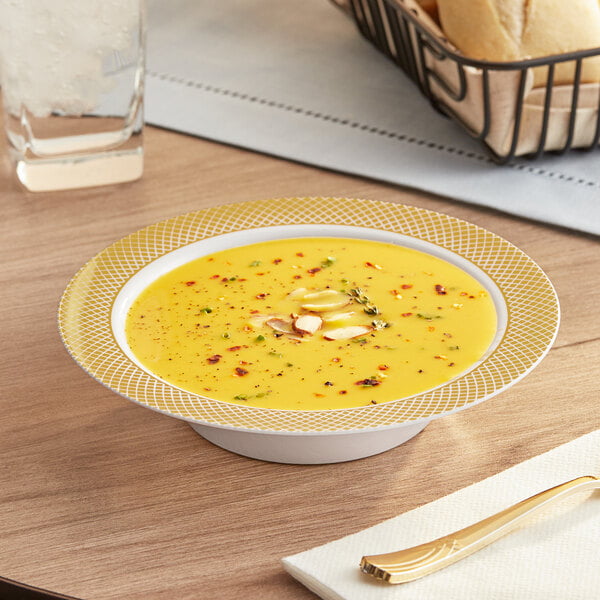 A Visions white bowl with a gold lattice design filled with soup on a table.