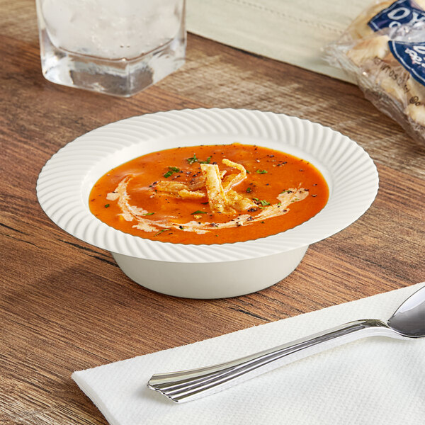 A Visions ivory plastic bowl filled with soup on a table with a silver spoon.