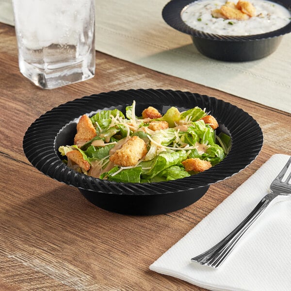 A bowl of salad in a black Visions plastic bowl on a table.