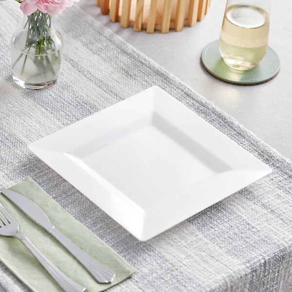 A white square Visions Florence plastic plate with a fork and knife on a table.