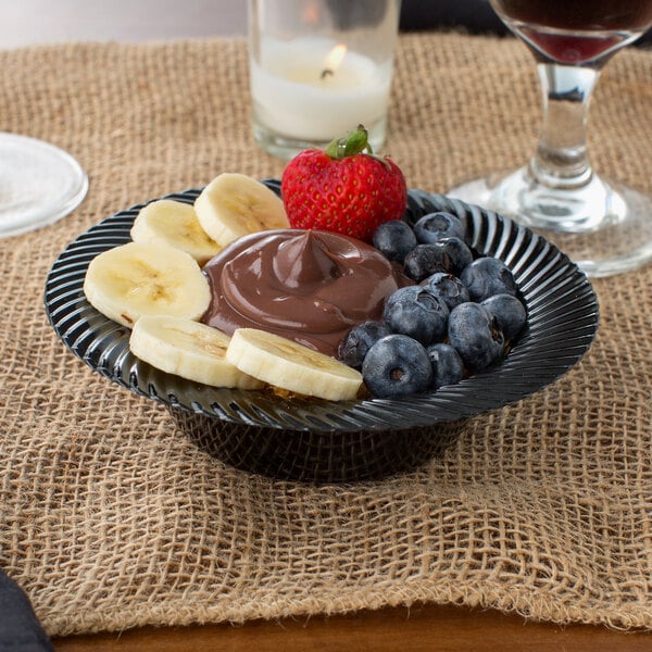 Chocolate pudding with sliced bananas, blueberries, and a strawberry in a black plastic bowl