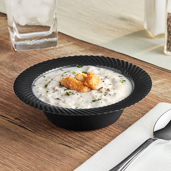 A Visions black plastic bowl filled with soup on a table with a spoon and napkin.