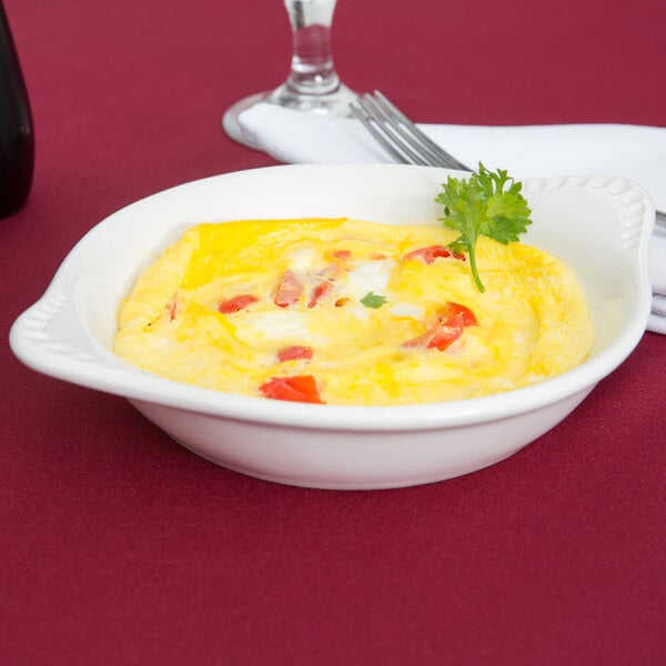 A white Tuxton round china dish with a shirred egg inside garnished with tomatoes and parsley.